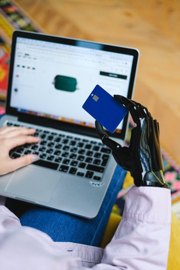 Person with prosthetic hand using laptop for online shopping, holding a credit card.